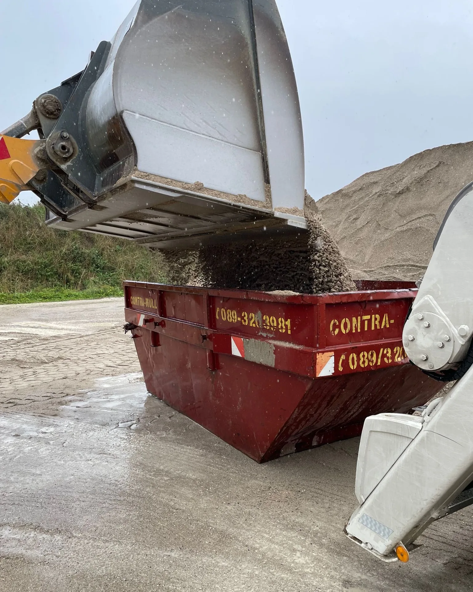 Bagger belädt einen Absetzcontainer von Contra Müll mit Erdaushub